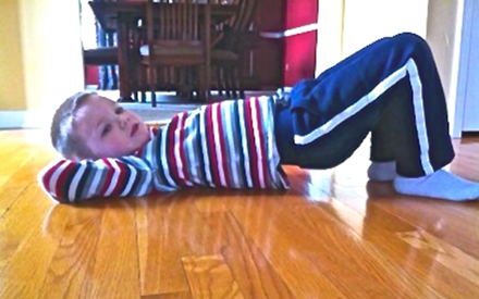 A child laying on his back on the floor doing a bridge exercise.