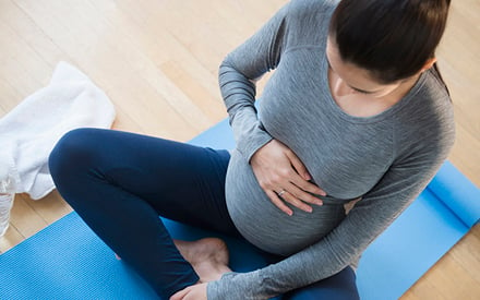 Pregnant woman sitting on yoga mat.
