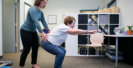 Patient squatting while physical therapist provides instruction.